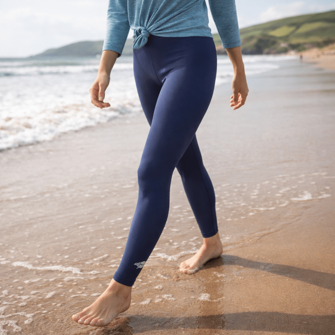 Woman walking on the beach wearing UPF 50+ sun-blocking swim leggings in navy