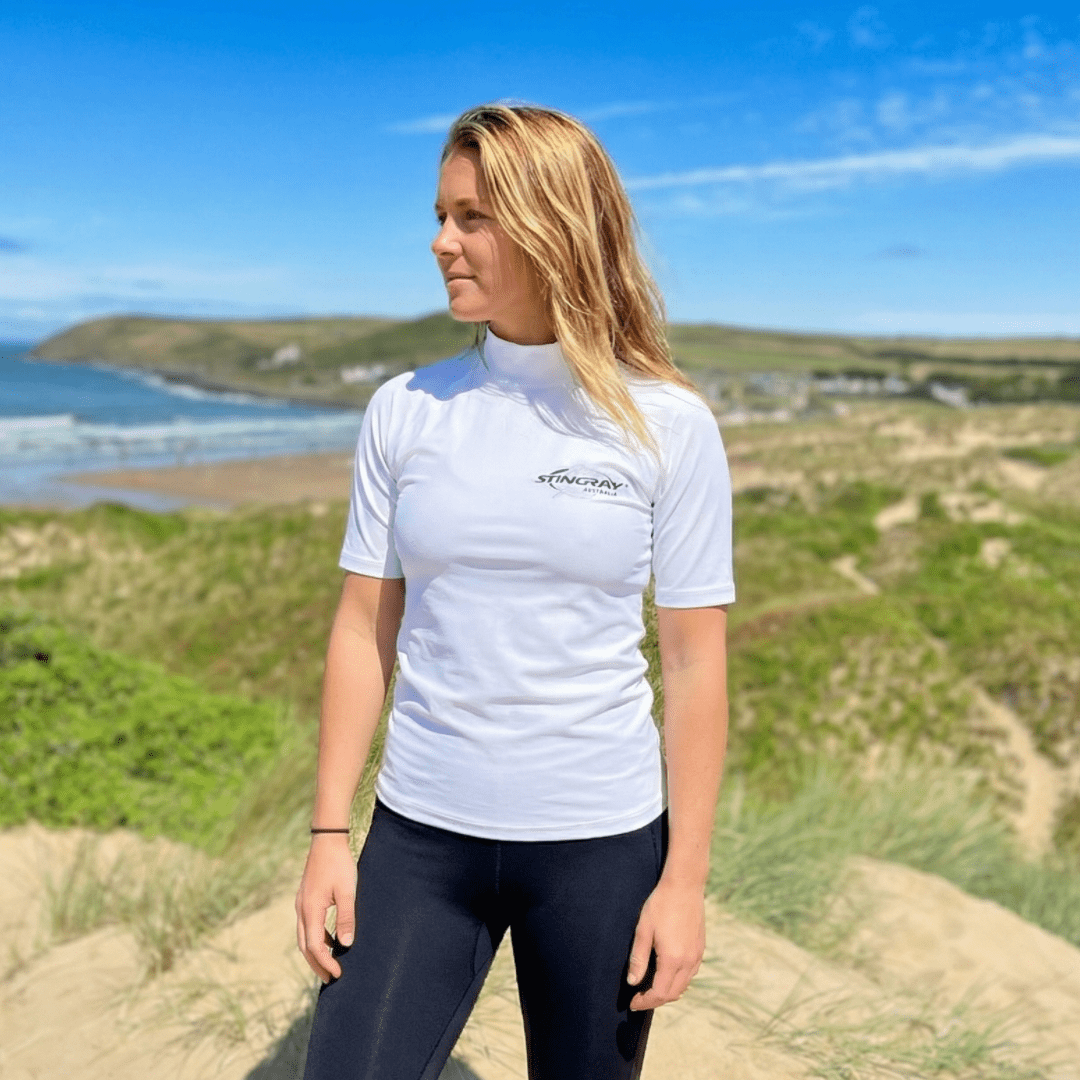 Woman wearing a white UV swim shirt with a Stingray logo on a beach