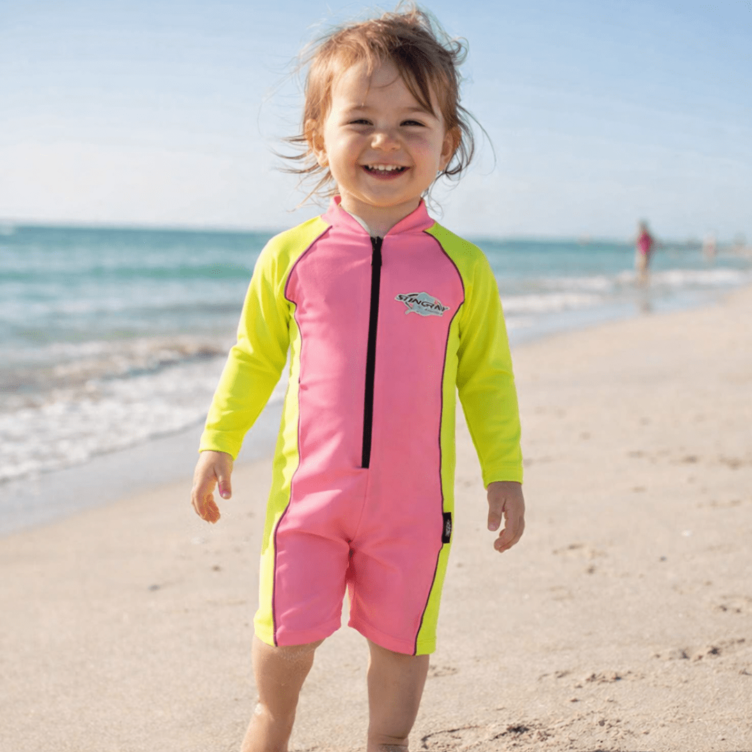 2 year old toddler wearing a long-sleeve UV sunsuit on the beach