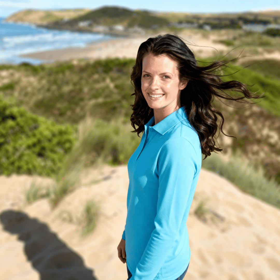 Woman in a blue long sleeve sun protection polo shirt standing on a sandy dune with a scenic background