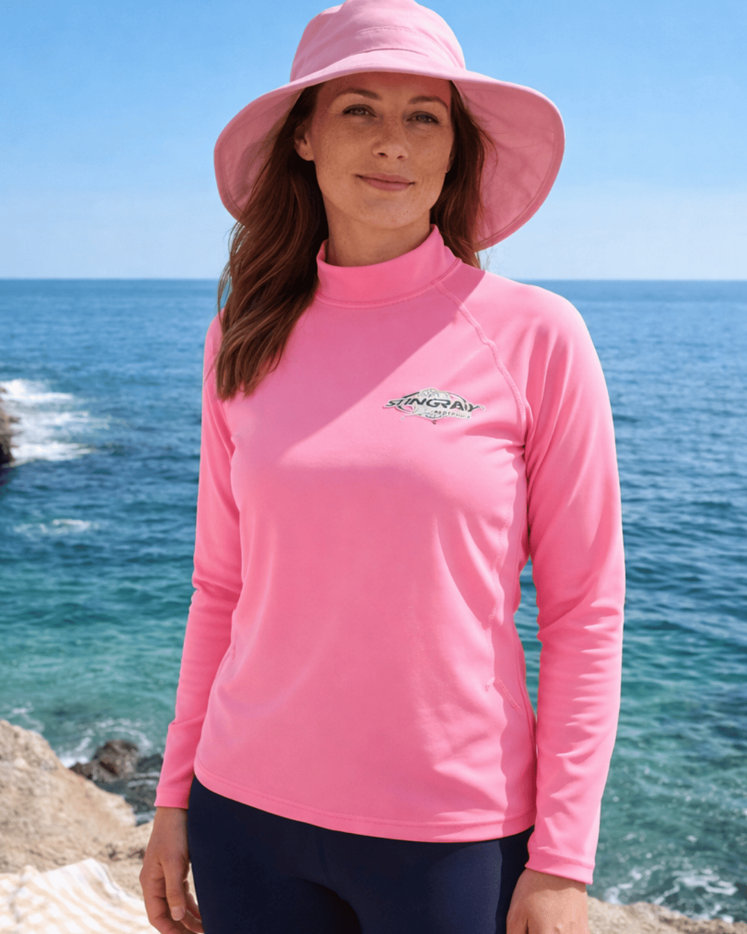 Woman wearing a pink UPF 50+ long-sleeve sun shirt and sun hat by the ocean
