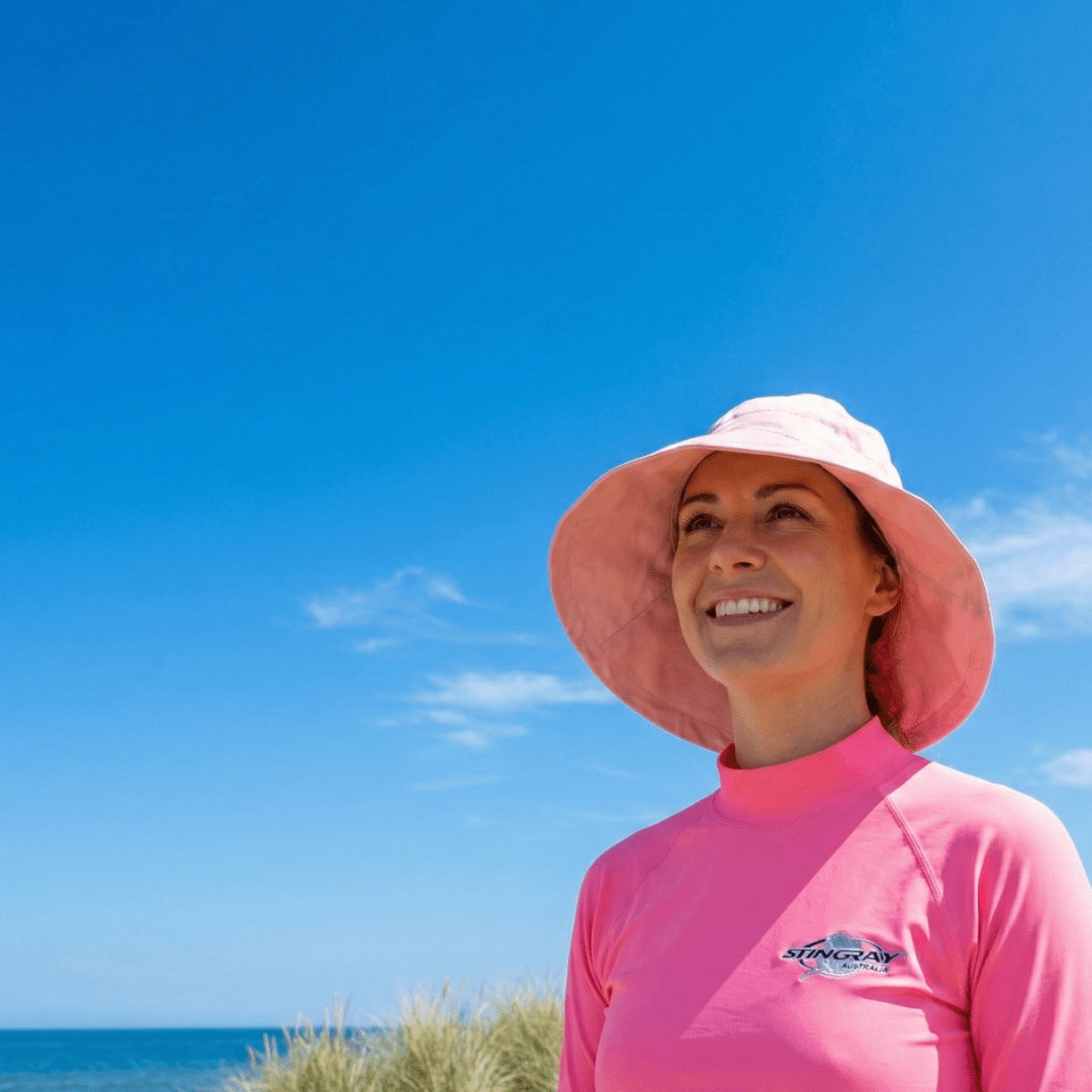 Woman wearing UPF swimwear and clothing standing on a beach with blue sky and ocean.