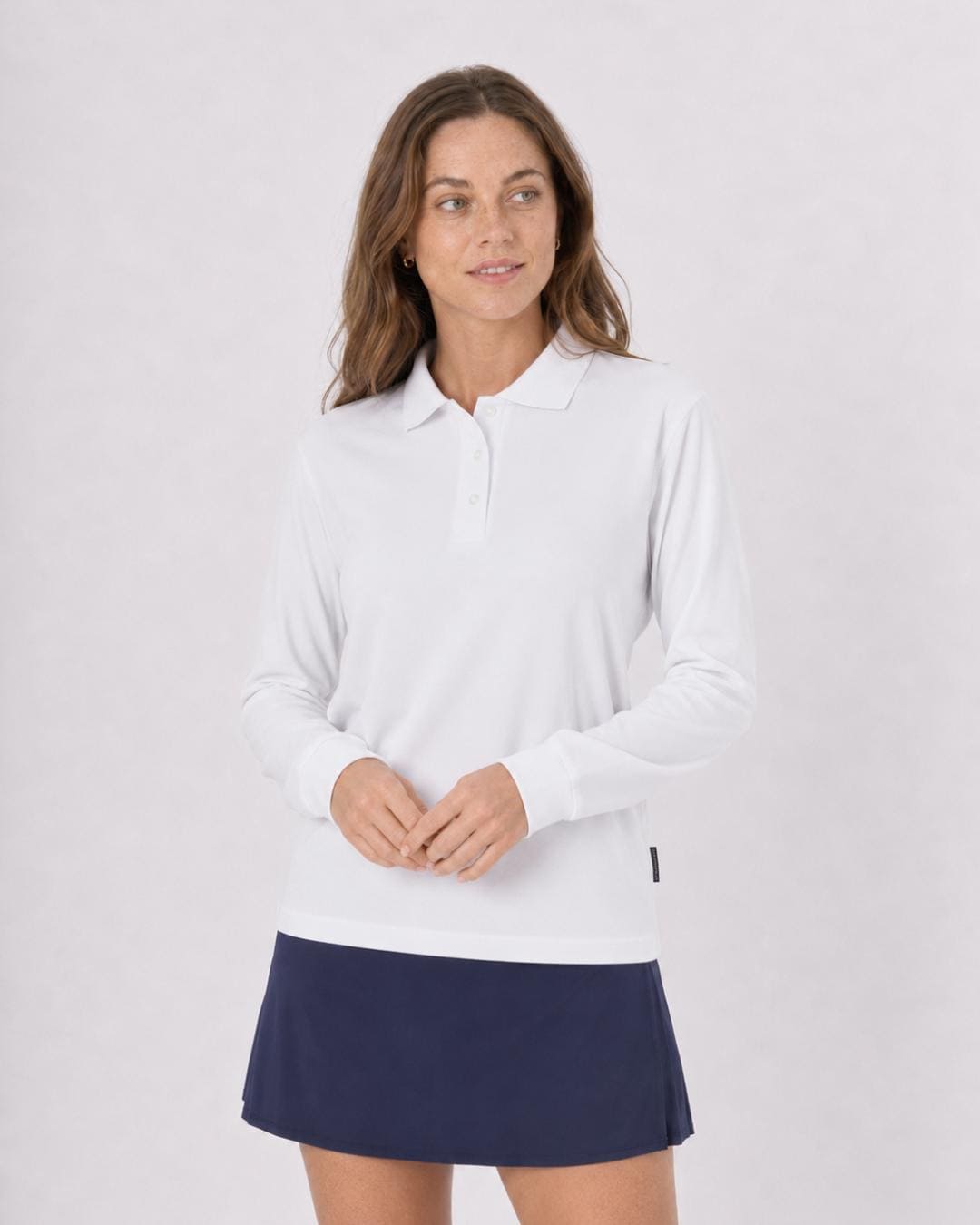 Woman wearing a white long-sleeve UV polo shirt UPF 50+ and tennis skort against a plain background